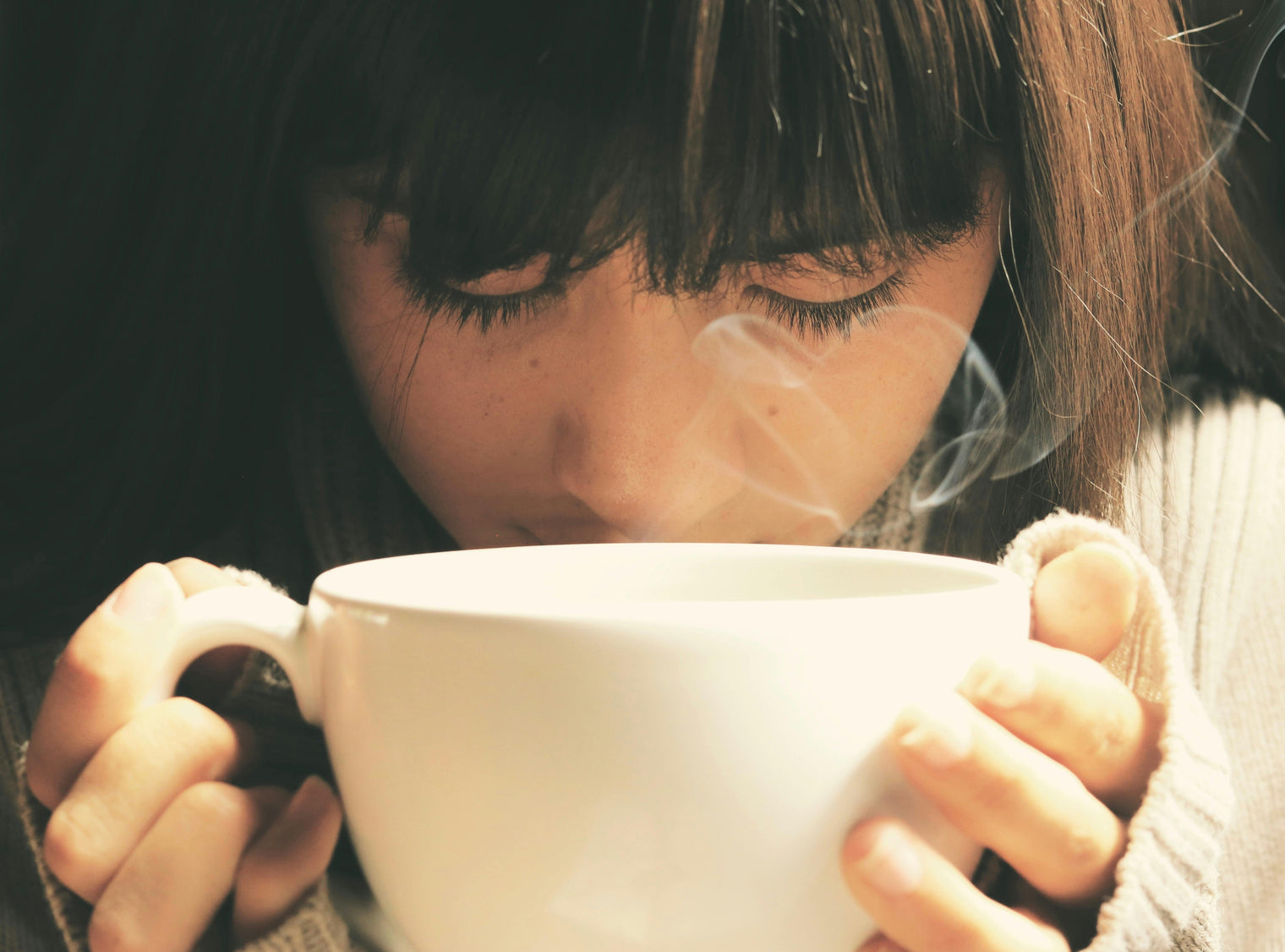 A woman smelling a large aromatic cup of tea.