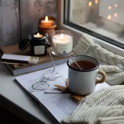 A cup of evening tea getting steeped next w a window next to two lit jar candles. 