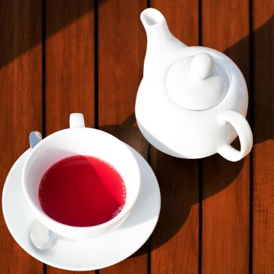 A white pot and a cup filled with hibiscus tea.