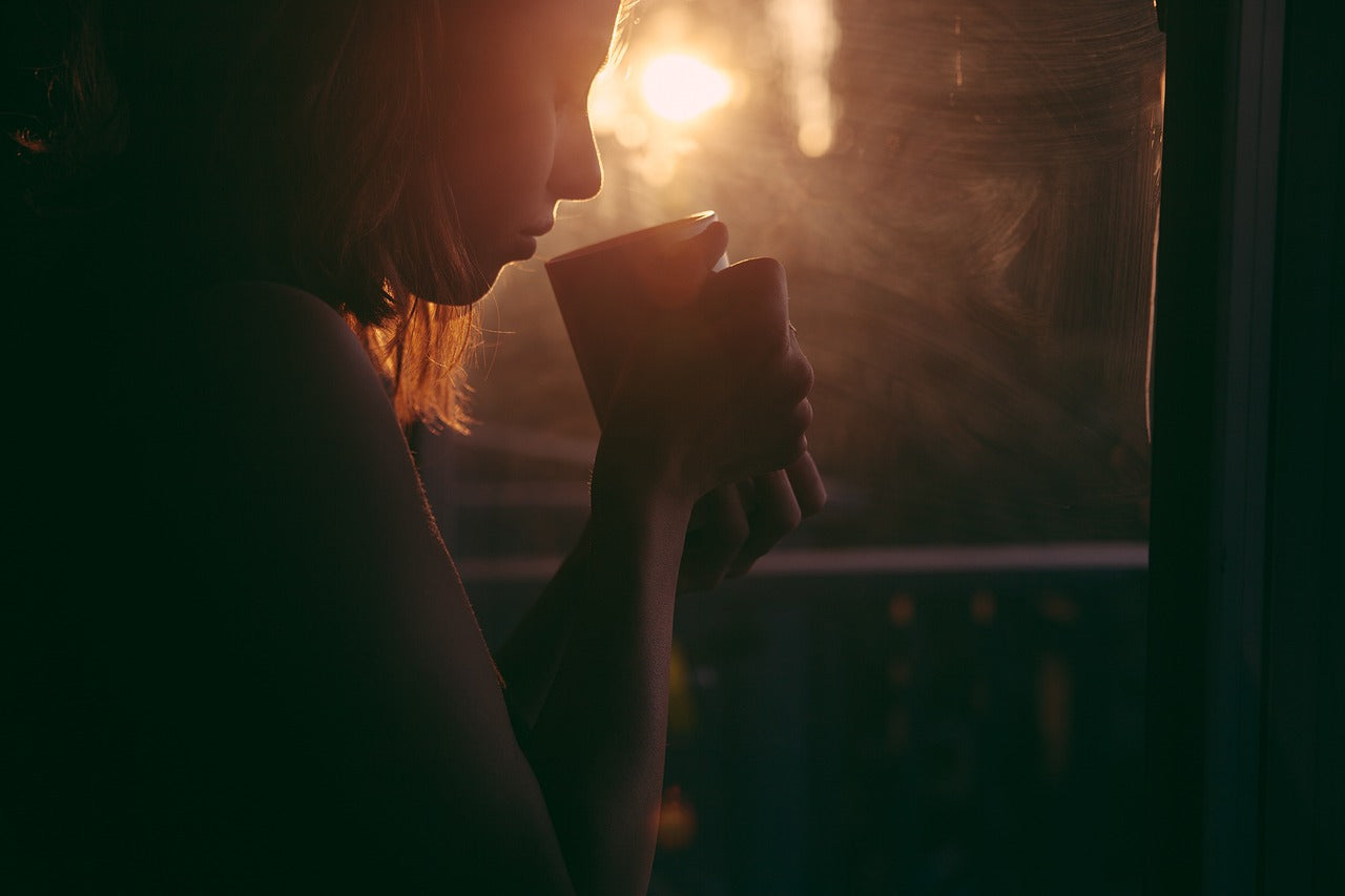 A woman drinking oolong  tea while the sun rises from the window beside her. 