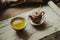 A pot next to a cup filled with green tea. 