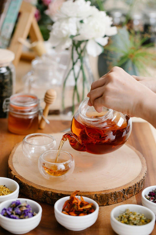 A clear teapot filled with herbal tea getting poured into a clear cup. 