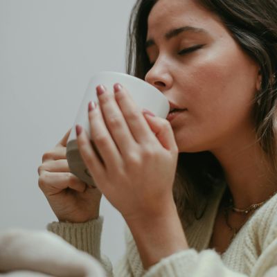 A woman closing her eyes and drinking a cup of tea for sore throat recovery.