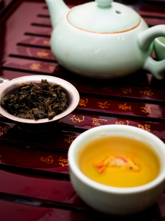 A pot of oolong tea next to a cup and steeped leaves. 